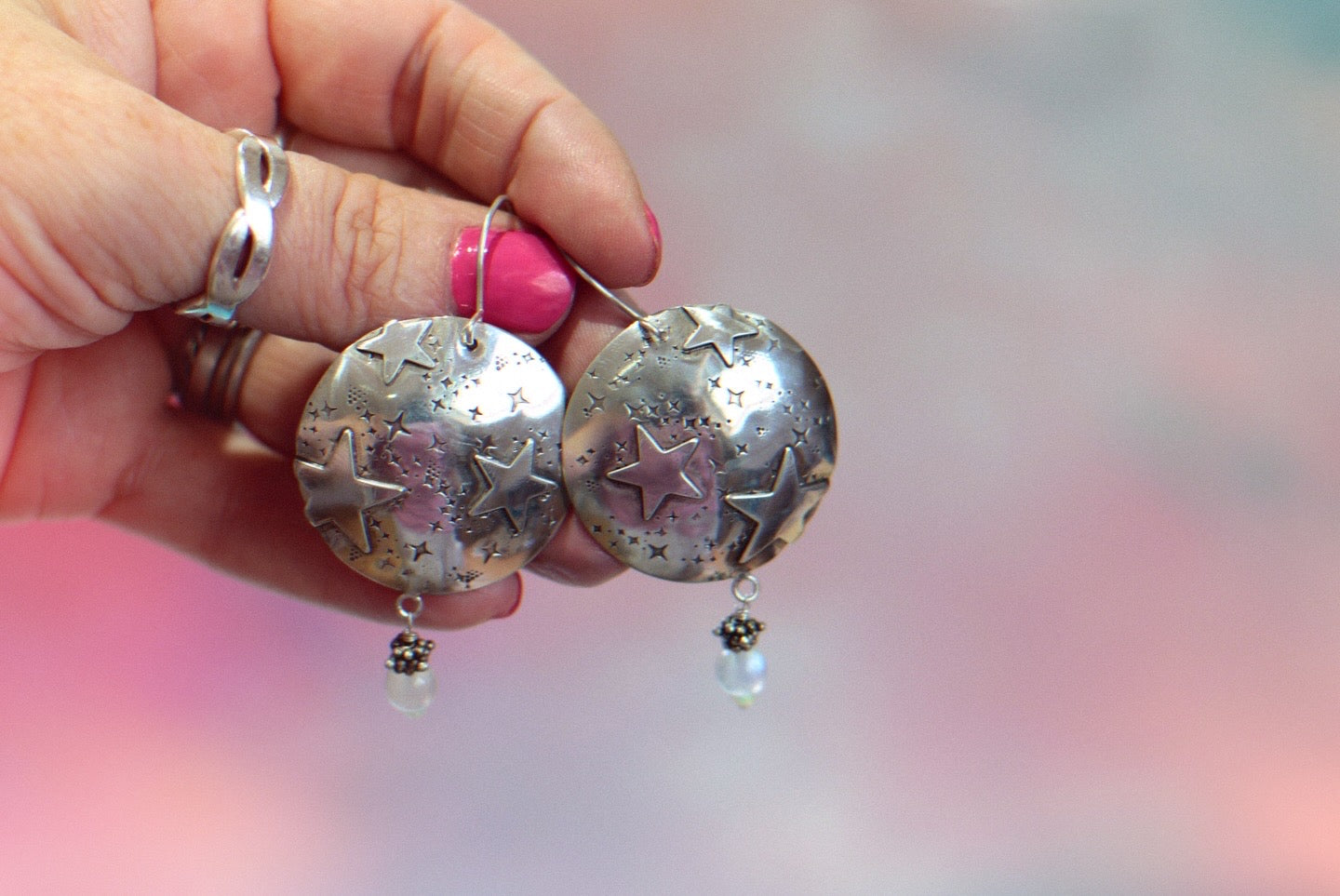 Silver earrings with star designs held by a hand against a blurred background