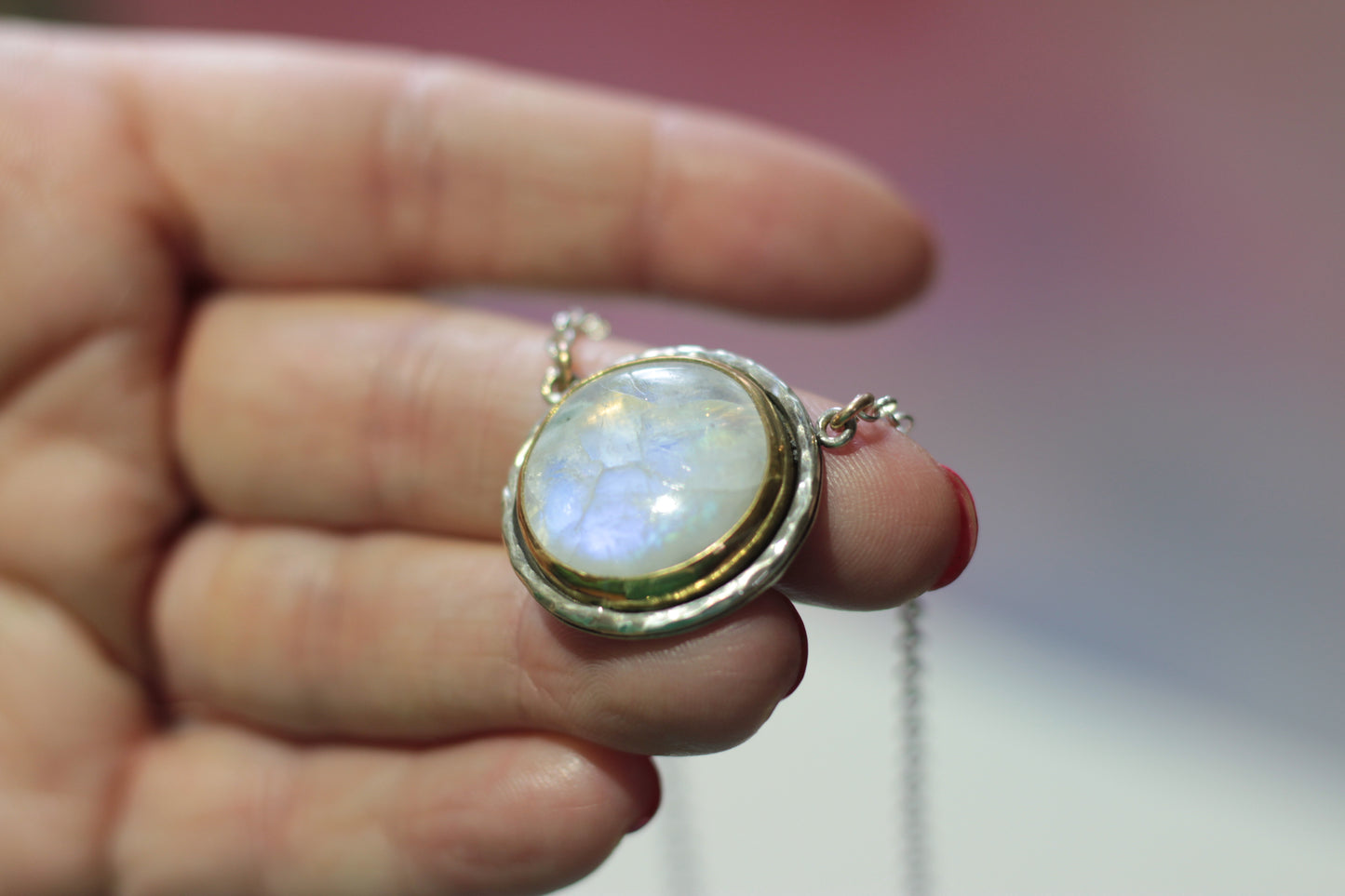 Hand holding a necklace with a pendant featuring a rainbow moonstone.