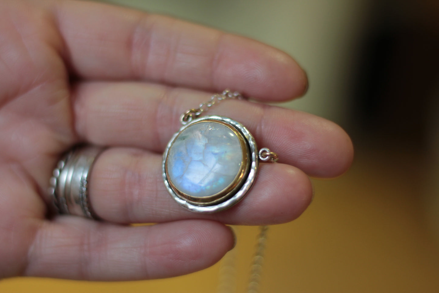 Hand holding a necklace with a moonstone pendant against a blurred background
