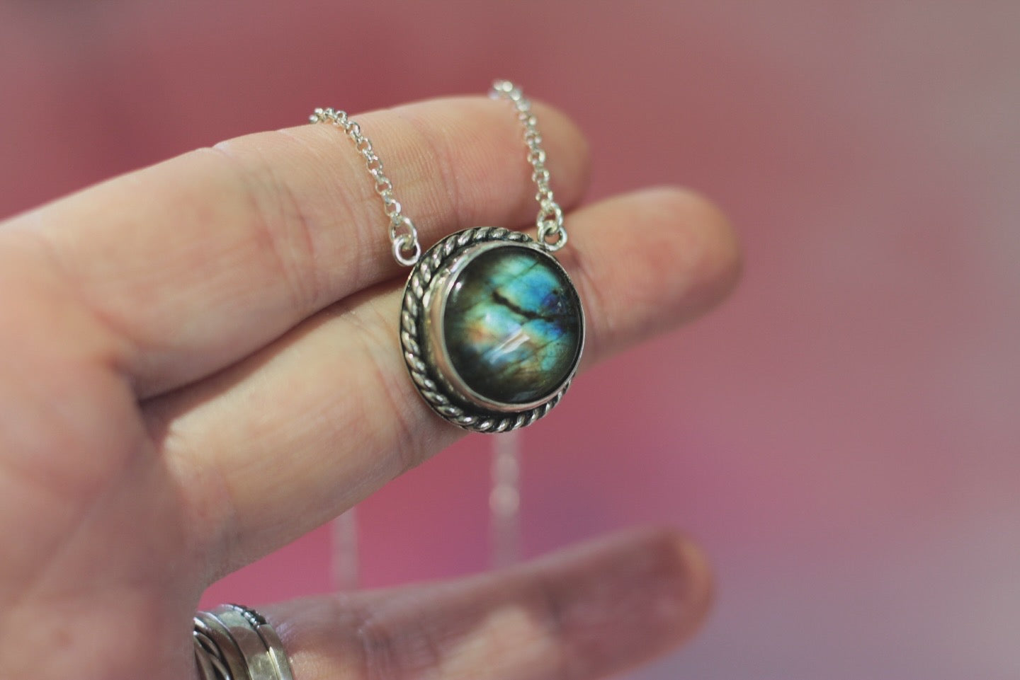 Necklace with a Labradorite pendant held by a hand against a blurred background