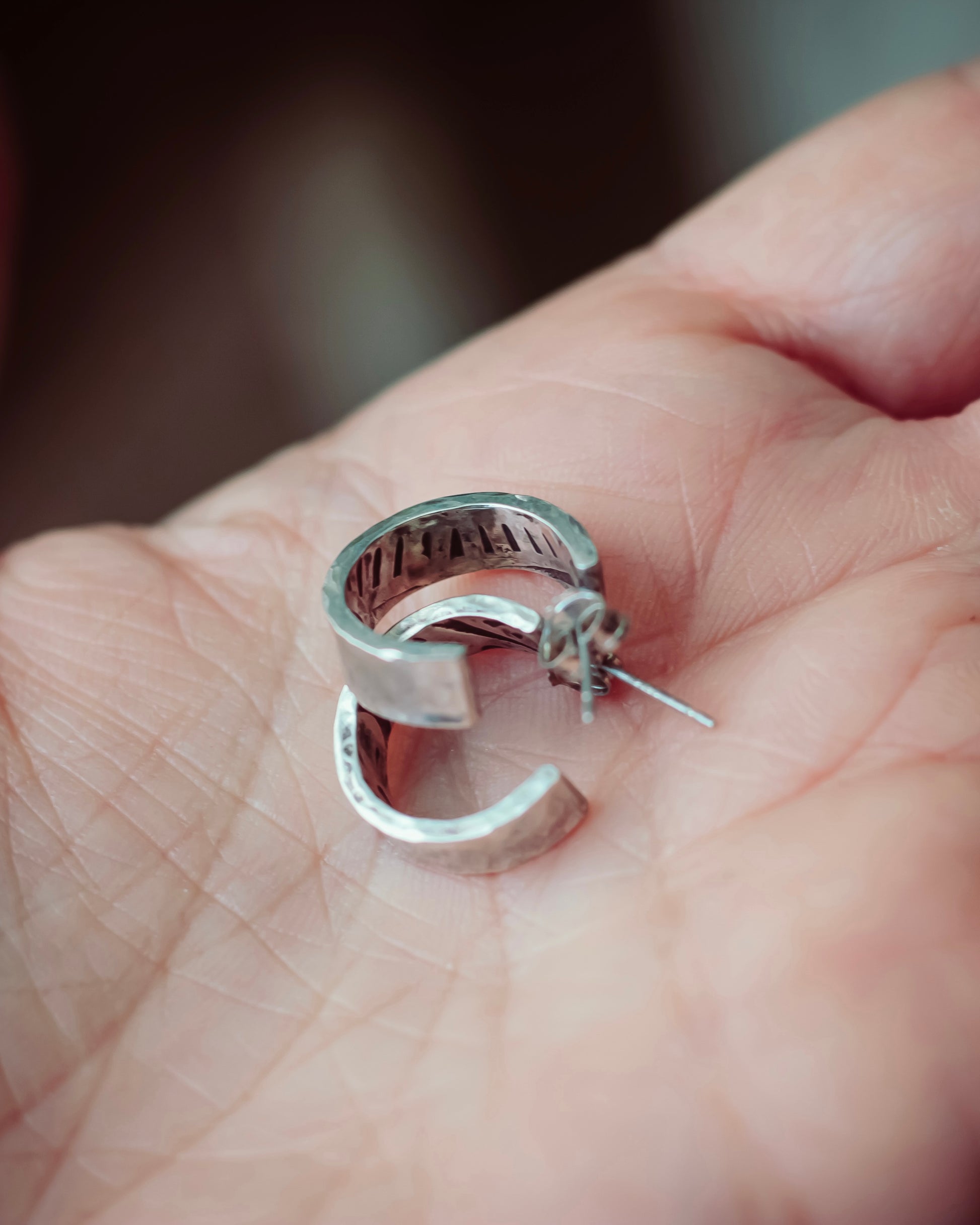 Hand holding sterling silver hoops with artisan detail is