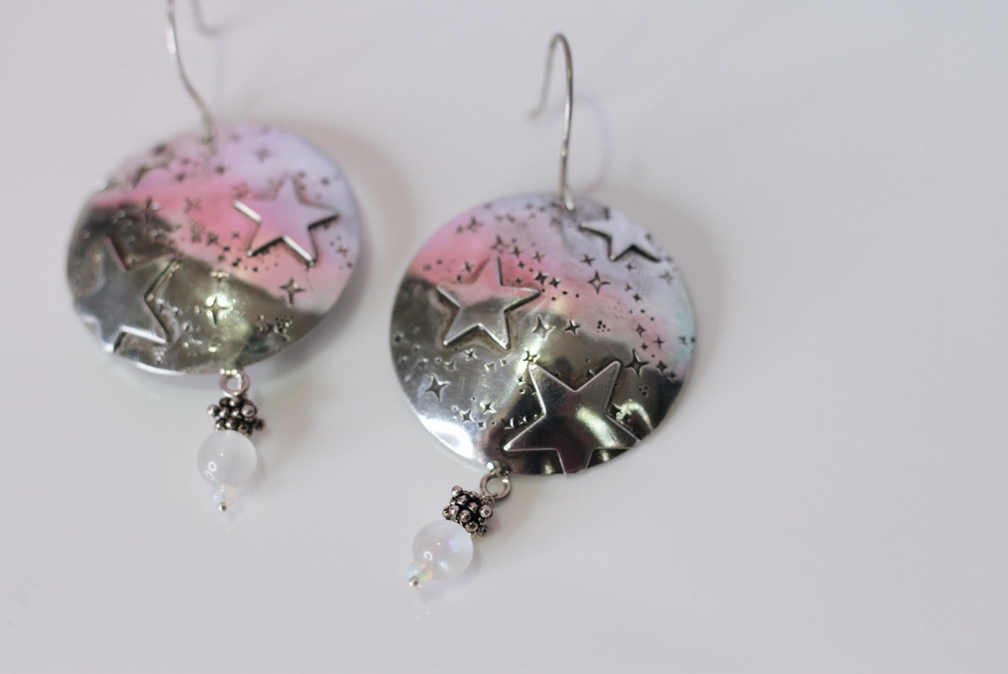 Pair of earrings with star and moon designs on a light pink background