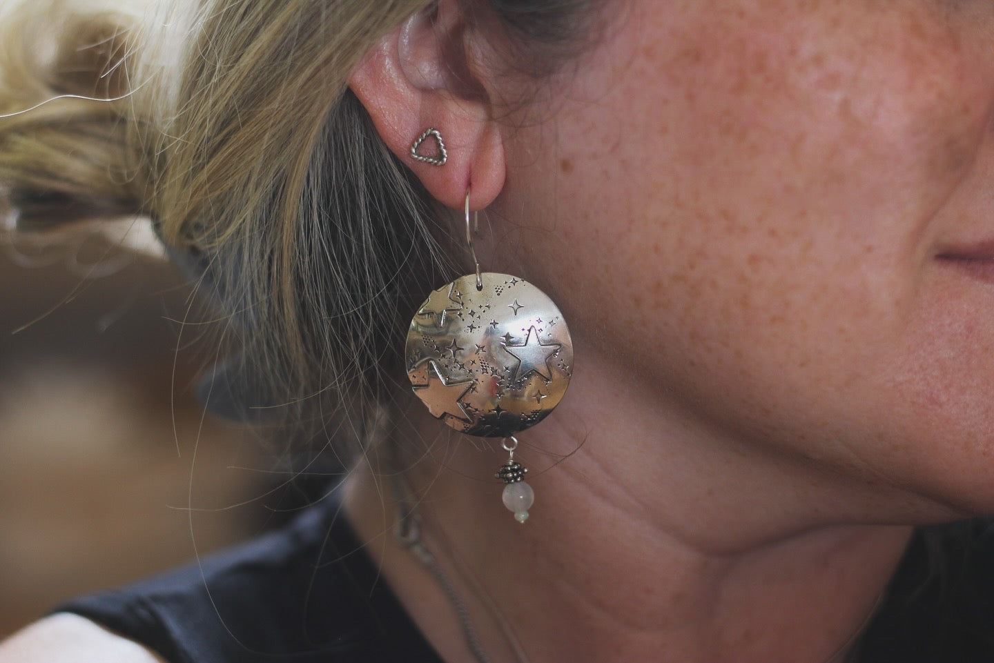 Close-up of a person wearing a silver earring with a textured ball design.