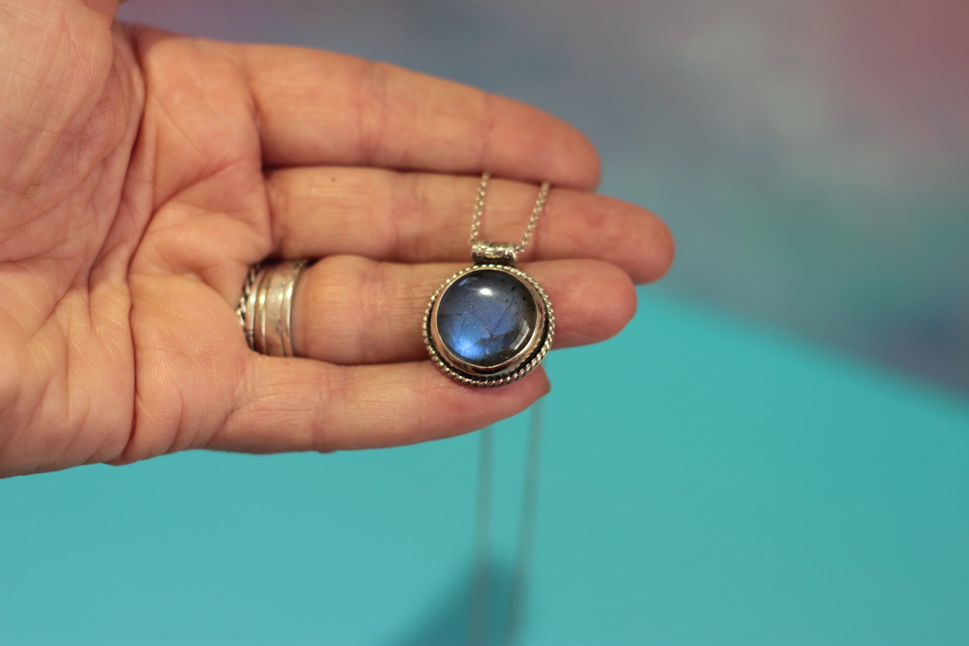 Hand holding a necklace with a blue labradorite stone pendant against a blurred background