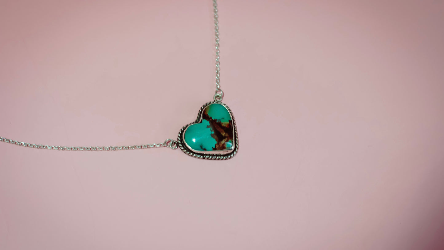 Turquoise heart-shaped pendant on a chain against a pink background