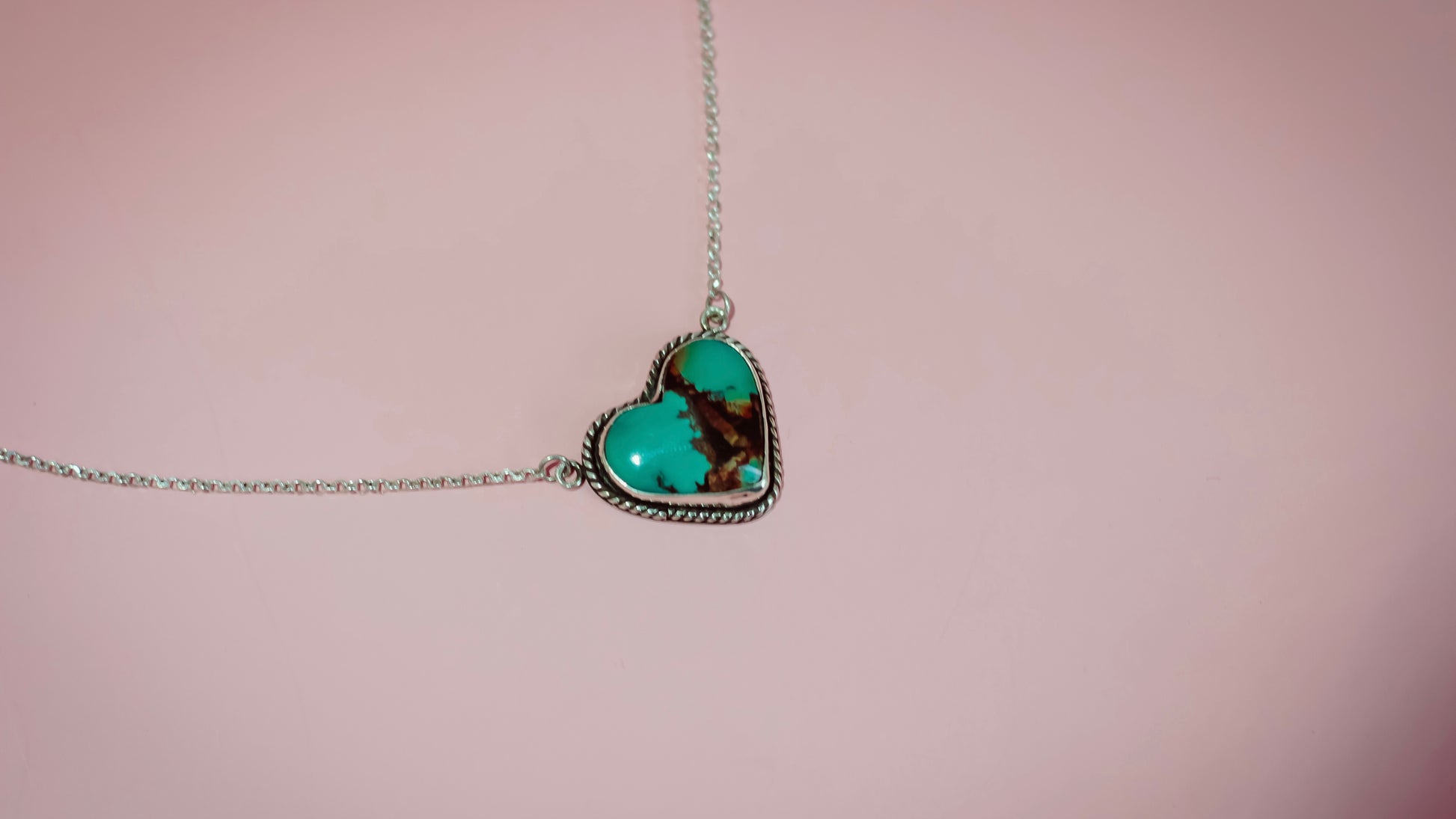Turquoise heart-shaped pendant on a chain against a pink background