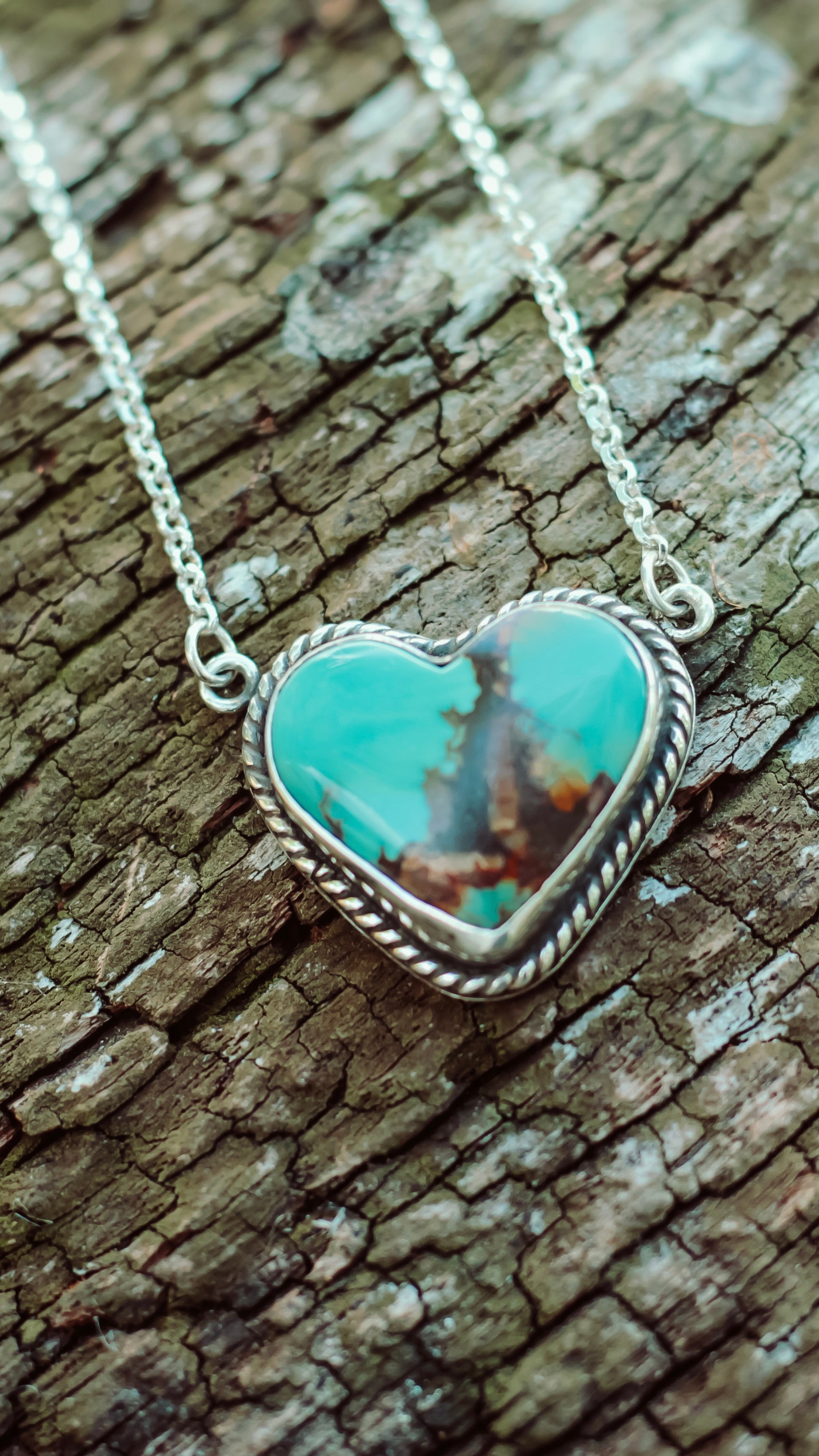 Turquoise heart-shaped pendant on a silver chain against a wooden background