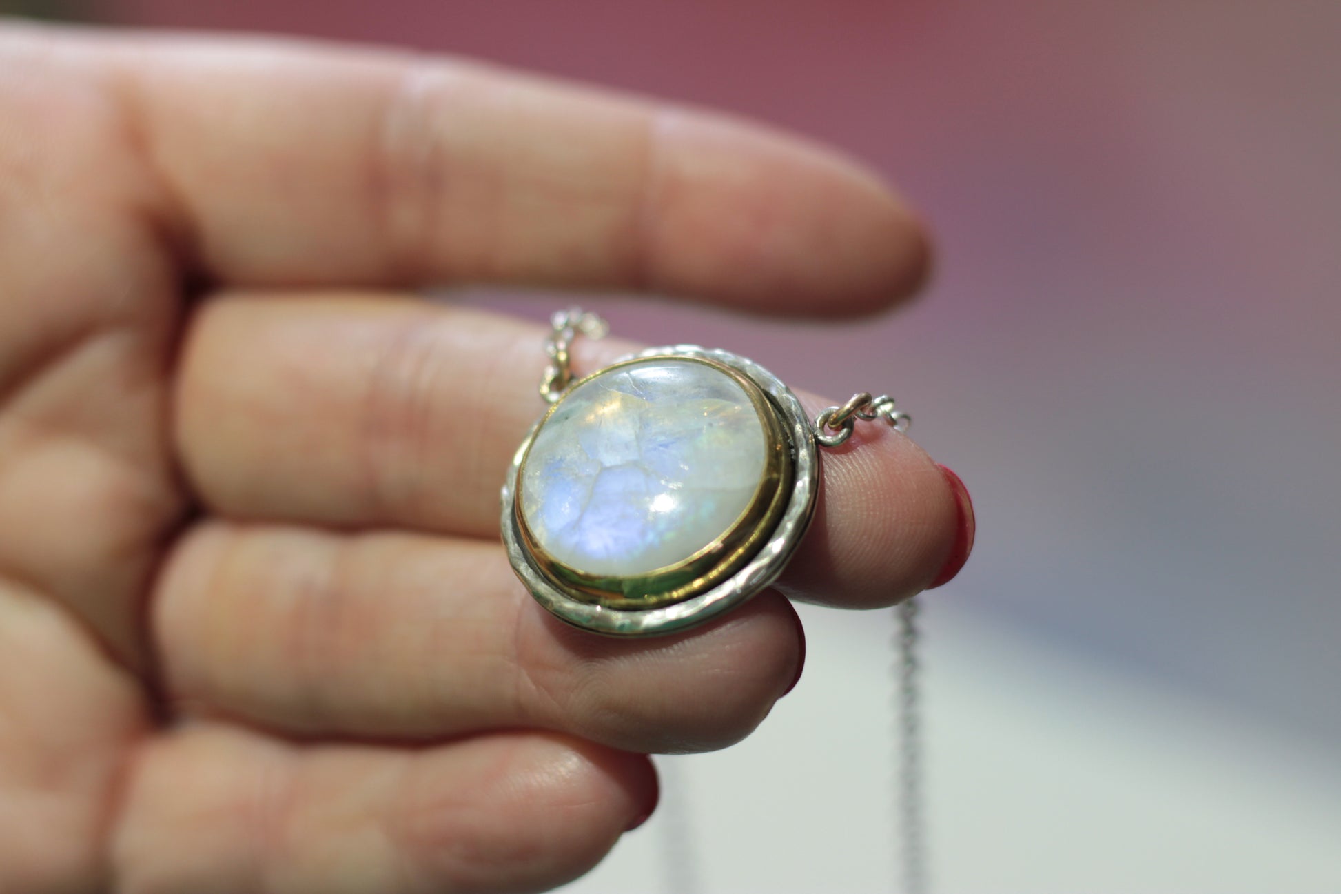 Hand holding a necklace with a pendant featuring a rainbow moonstone.