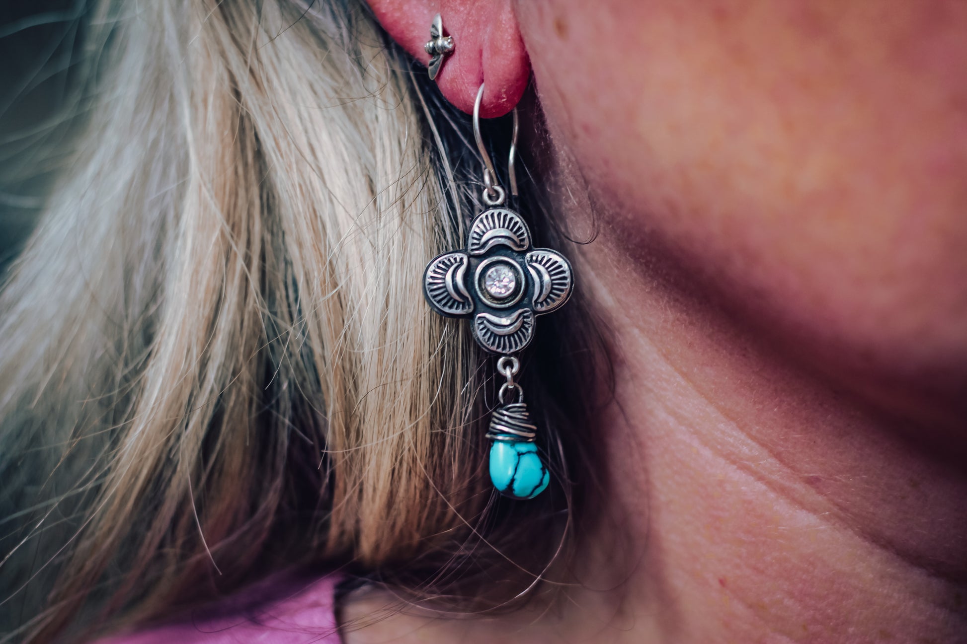 Close-up of a person wearing a silver earring with turquoise stones.