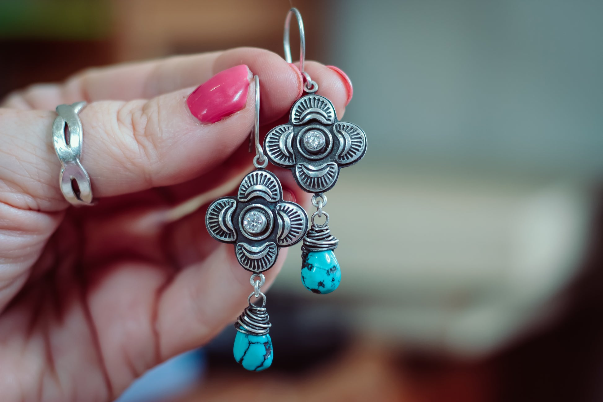 Hand holding silver earrings with turquoise drops against a blurred background