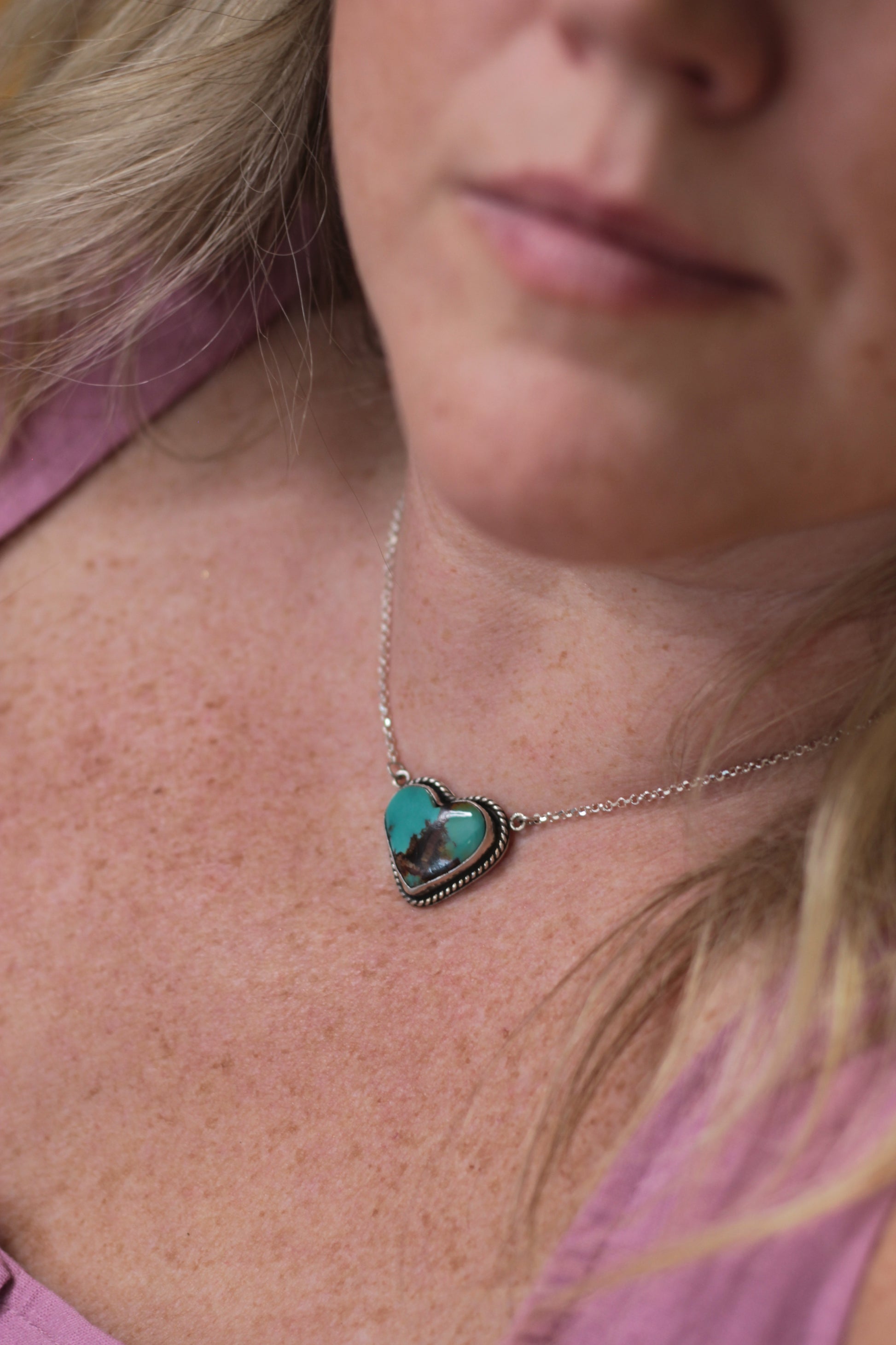 Close-up of a necklace with a heart-shaped pendant worn by a person.