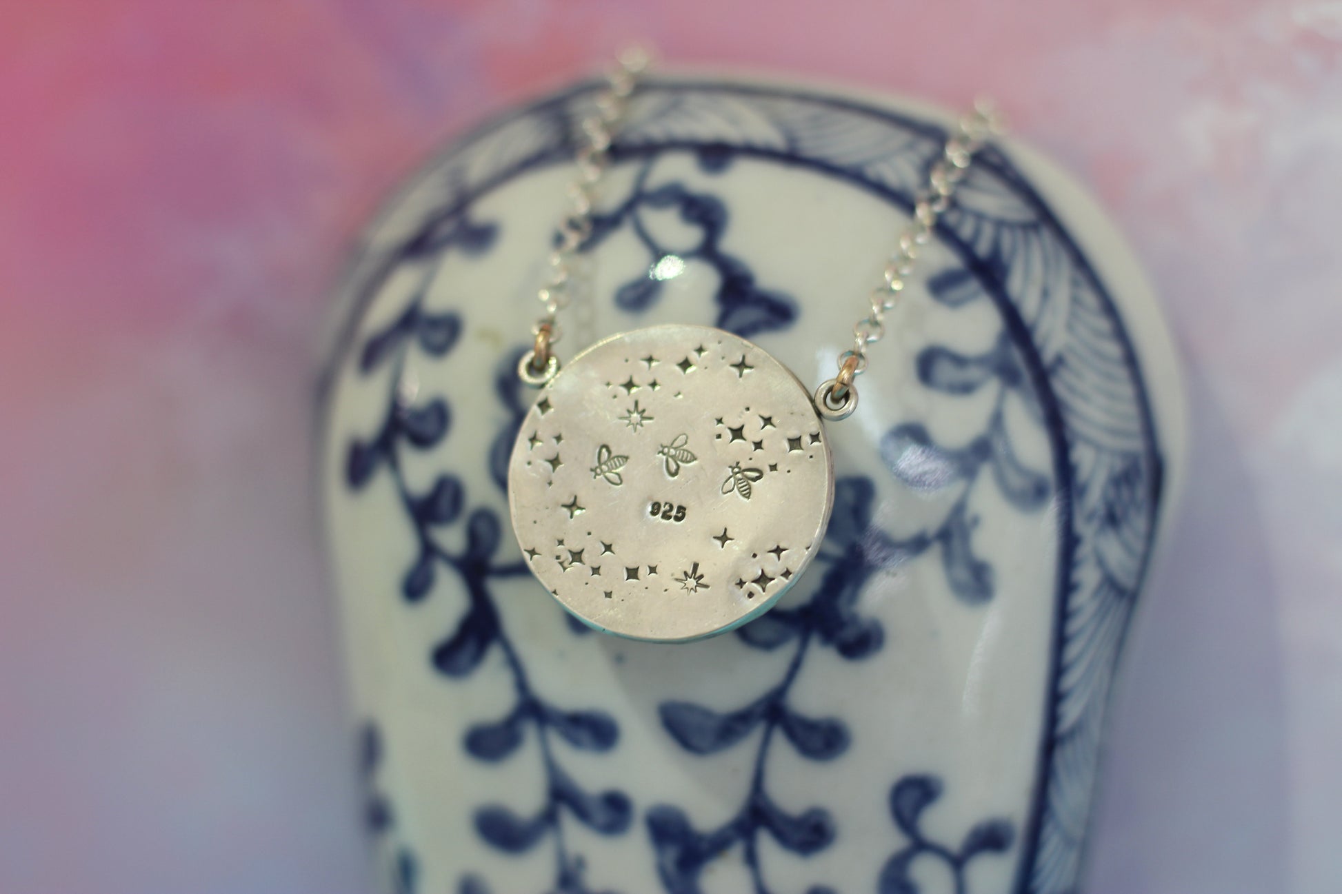 Gold necklace with a circular pendant on a decorative ceramic object with a pink and white background