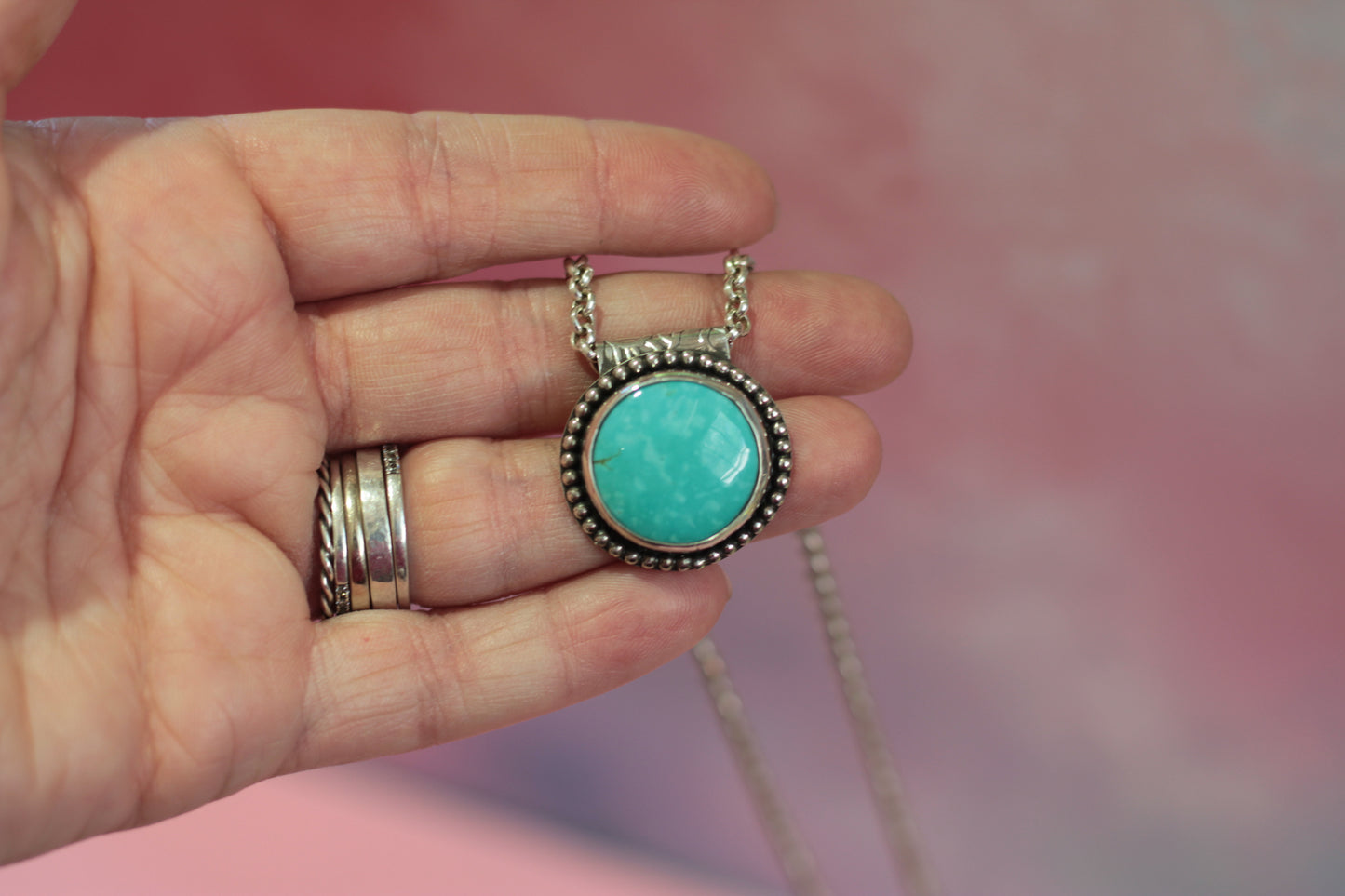 Turquoise pendant necklace held in a hand with pink background