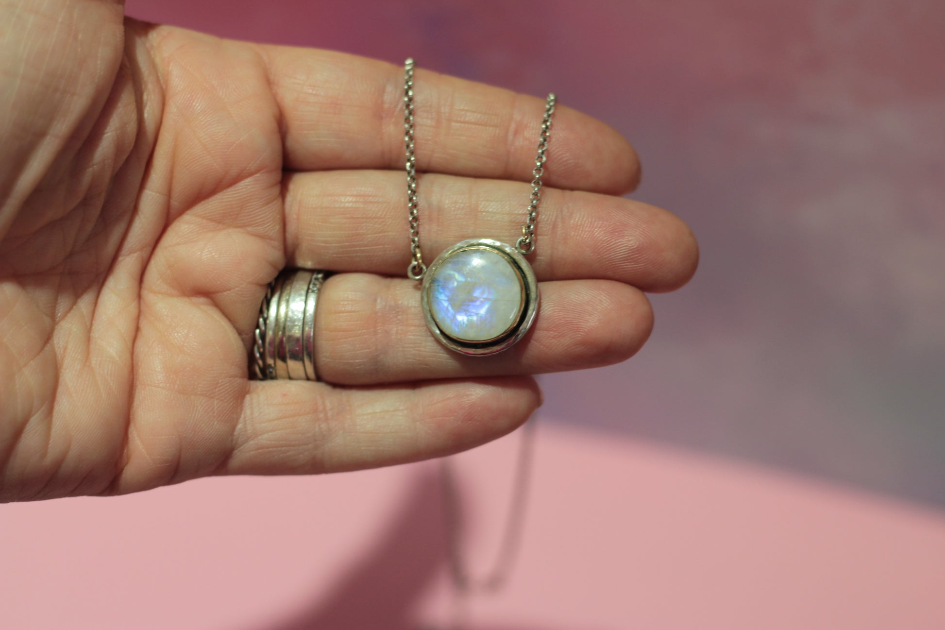 Hand holding a necklace with a glowing pendant against a pink background